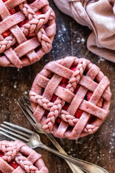 two small pies with strawberries on top next to silverware and fork, all covered in powdered sugar