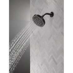 a shower head with water coming out of it's side and white tile on the wall