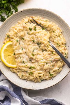 a white bowl filled with pasta and garnished with parsley on the side