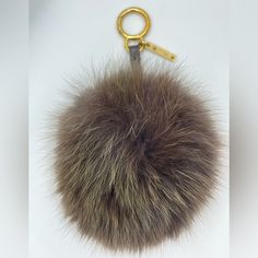 a fur ball keychain hanging from a gold metal hook on a white background