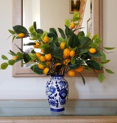 a blue and white vase filled with oranges sitting on top of a table next to a mirror