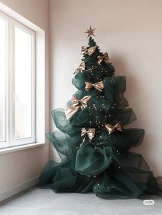 a green christmas tree with gold stars and bows on it in front of a window