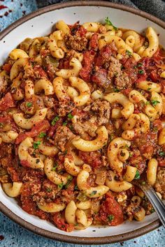 a bowl full of pasta with meat and tomato sauce on the side next to a fork