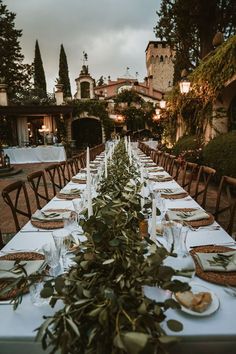 a long table is set with plates and place settings for an outdoor dinner in the evening