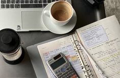 an open notebook with a calculator, coffee cup and pen on it next to a laptop