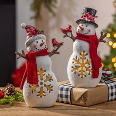 two snowmen standing next to each other on top of a wooden table near a christmas tree