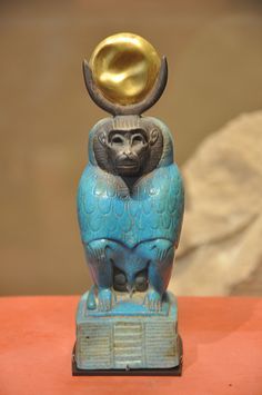 a statue of an owl with a golden disk on its head sitting on top of a table