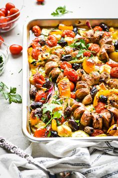 a casserole dish filled with meat, vegetables and tomatoes on a white table