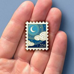 a hand holding a tiny stamp with the moon and clouds on it in front of a blue background