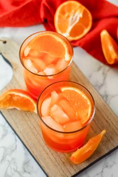 two glasses filled with orange juice sitting on top of a cutting board next to sliced oranges