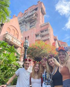 three girls and one boy are posing in front of a building with flowers on it