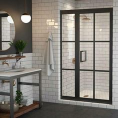 a white tiled bathroom with black trim and glass shower door, sink, mirror and towel rack