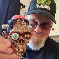 a man with glasses and a hat is holding a fake zombie head in his hand