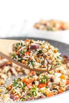 a spoon full of rice and vegetables being lifted from a skillet with another dish in the background