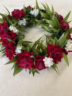 a wreath made out of red and white flowers sitting on a bed with green leaves