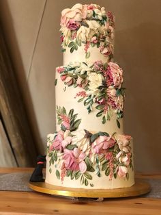 a three tiered wedding cake with pink and white flowers on the top, sitting on a wooden table