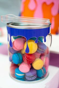 a jar filled with colorful macaroni and cheese covered in blue paint sitting on top of a table