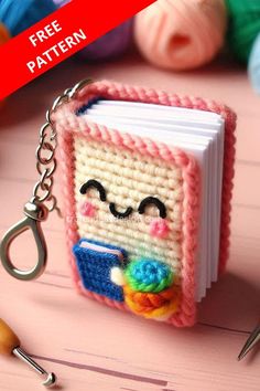 a book shaped keychain is sitting on a table with knitting needles and yarn