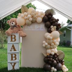 a teddy bear sitting on top of a sign with balloons attached to it's sides