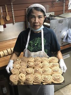 a man in an apron holding a pan filled with rolled up doughnuts and looking at the camera