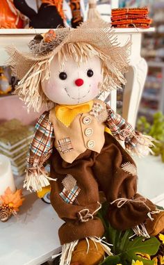 a scarecrow doll sitting on top of a table next to flowers and pumpkins