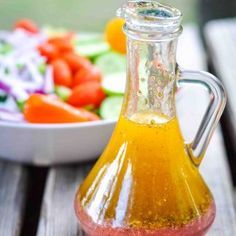 a glass bottle filled with liquid sitting on top of a wooden table next to a bowl of vegetables