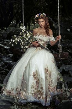 a woman in a white dress is sitting on a swing with flowers and greenery