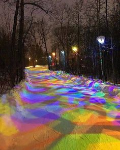 the snow is covered with colored lights and trees in the background, along with street lamps