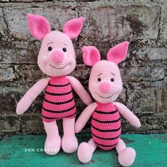 two pink crocheted pigs sitting next to each other on a green bench with brick wall in the background