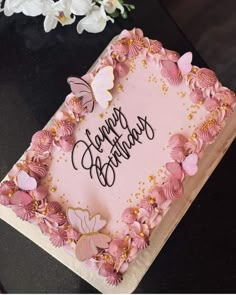 a birthday cake with pink frosting and butterflies on it, surrounded by white flowers