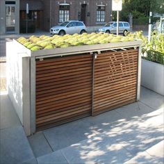 a wooden fence with plants growing on top and cars parked in the background behind it