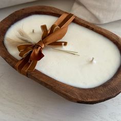 a white candle with a brown bow in a wooden bowl on a table next to a pillow