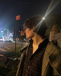 a young man standing on the side of a road at night with his hand out