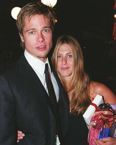 a man in a suit and tie standing next to a woman holding a gift bag