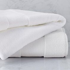 two white towels stacked on top of each other in front of a marble wall and floor