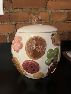 a ceramic jar with buttons and leaves painted on the side, sitting on a table