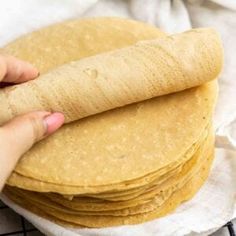 a stack of tortillas sitting on top of a white towel next to a person's hand