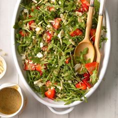 a salad in a white bowl with two wooden spoons next to it on a table