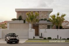 a car is parked in front of a house with palm trees on the side walk