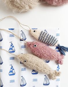 three knitted fish ornament sitting on top of a white table next to some balls of yarn