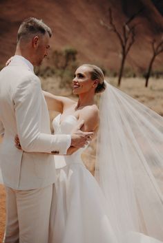 a bride and groom are standing in the desert with their veil blowing in the wind