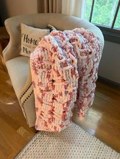 a pink blanket sitting on top of a chair in front of a window with a pillow