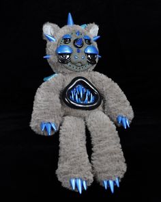 a stuffed animal with blue and black decorations on it's face, sitting in front of a black background