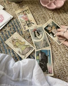 a person's hand on top of some cards next to a pink teapot