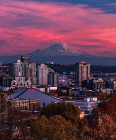 the city skyline is lit up at dusk with a mountain in the background and pink clouds