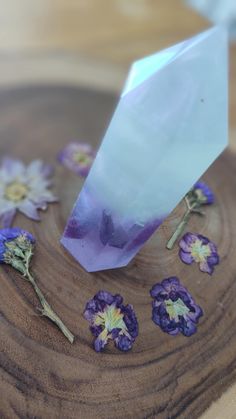 purple and white flowers are on a wooden plate with a plastic bag over it that is sitting on top of the wood