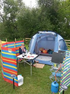 an outdoor tent set up in the grass with two people sitting at a picnic table