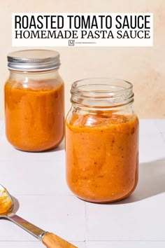 two jars filled with homemade tomato sauce on top of a white counter next to a spoon