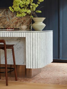 a vase with flowers sitting on top of a marble counter next to two stools