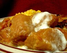 a white plate topped with meatballs covered in sauce and cream next to corn on the side